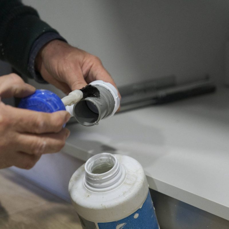 Mature plumber hands applying glue to a grey plastic pipe. Repairman working.